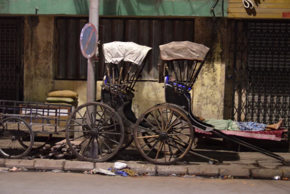 Two hand-pulled rickshaws parked against a weathered building with canvas canopies