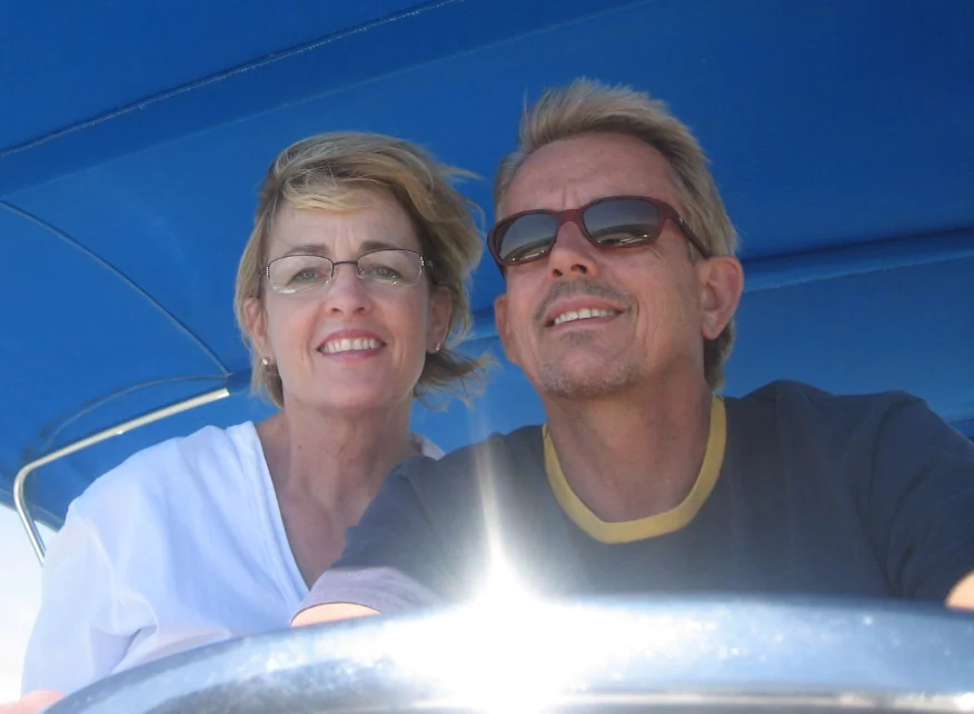 Two smiling people posing together against a bright blue background with sunlight reflections.