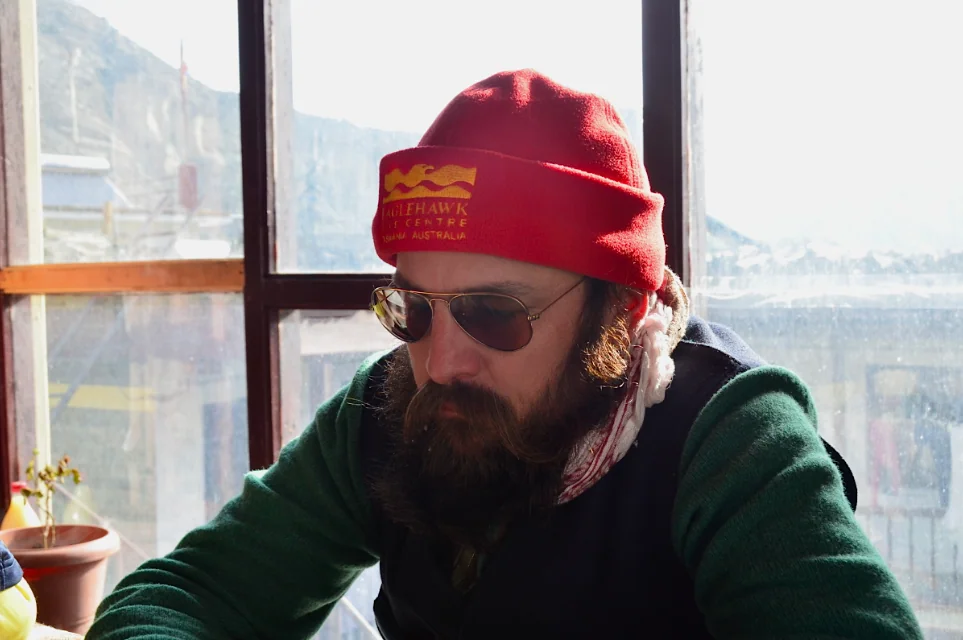 Man wearing red beanie and sunglasses by window overlooking mountain landscape