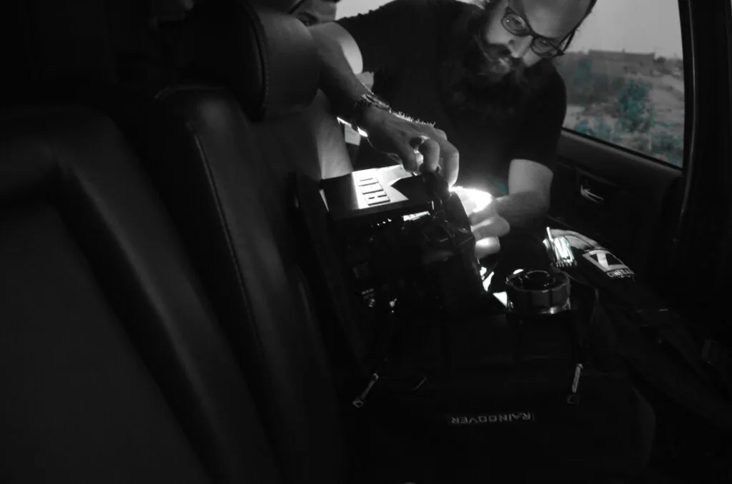 Person wearing glasses sits in vehicle interior holding mobile device with landscape visible through window