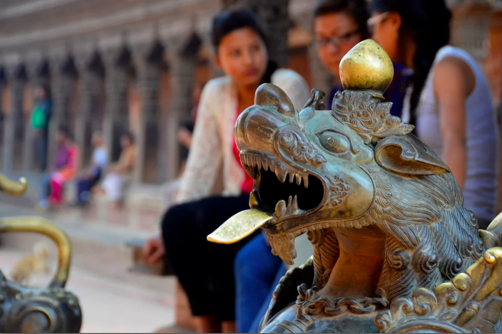 Bronze dragon statue with golden sphere in foreground, blurred visitors and temple architecture in background