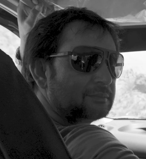 Man wearing sunglasses seated in vehicle interior, black and white photograph