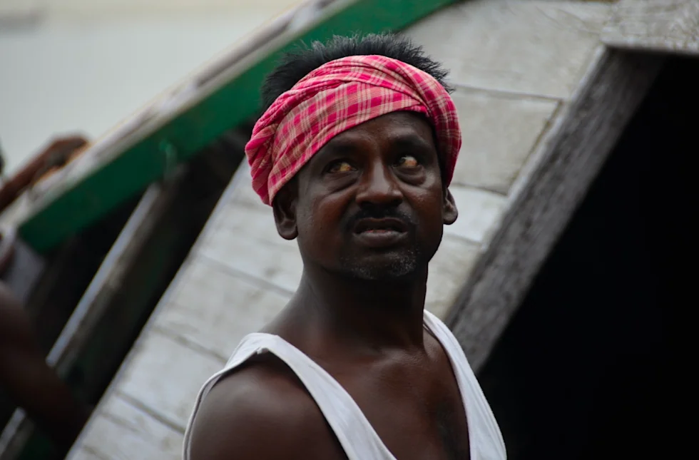Man wearing pink checkered headwrap and white sleeveless shirt looking upward