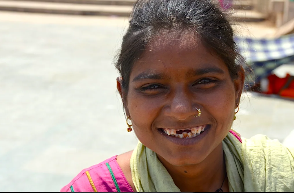 Young woman smiling at camera wearing pink and green clothing with nose ring and earrings
