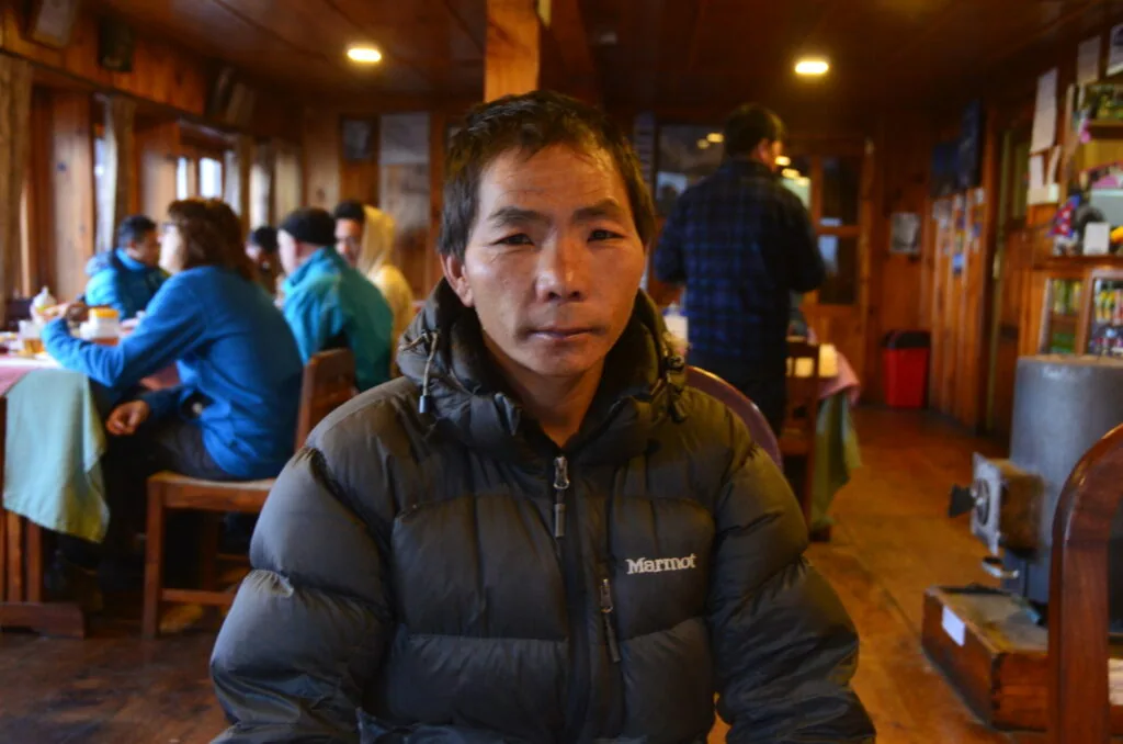Man wearing black puffer jacket inside wooden lodge with other people in background