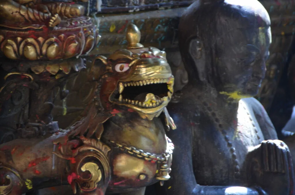 Ornately decorated wooden demon mask with gold teeth and jeweled collar alongside dark sculptured head