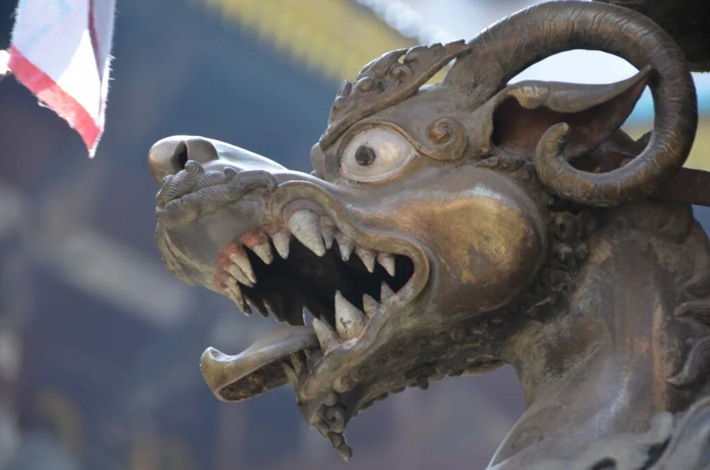 Bronze ornamental dragon sculpture with curled horns, open mouth displaying sharp teeth, and decorative details