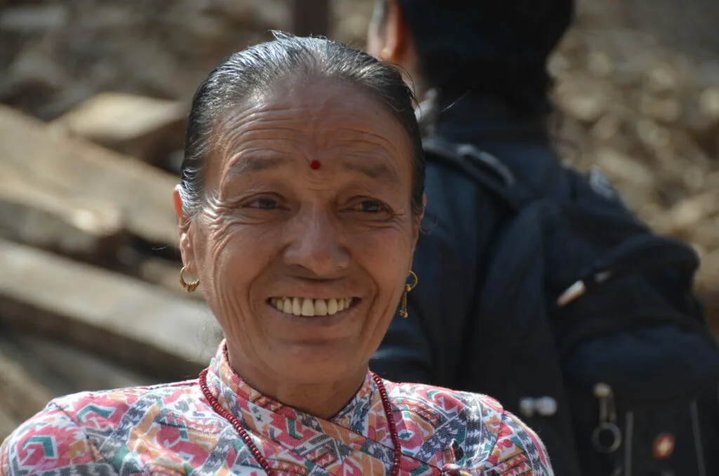 Smiling woman with red bindi wearing colorful patterned shirt with gold earrings