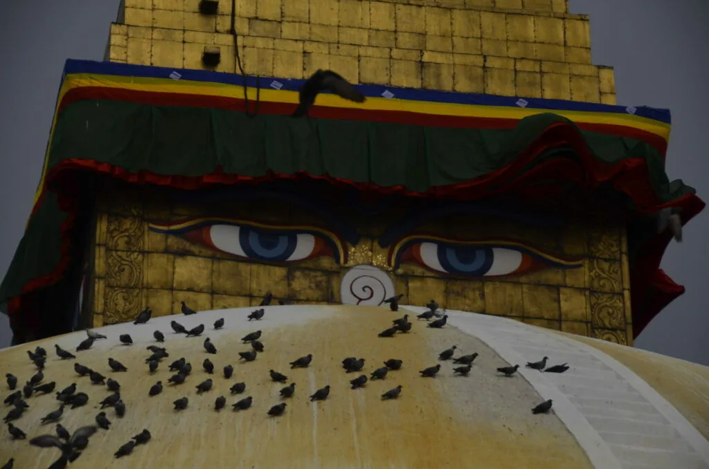 Large statue with painted blue eyes, spiral mark, and birds perched on white curved surface below