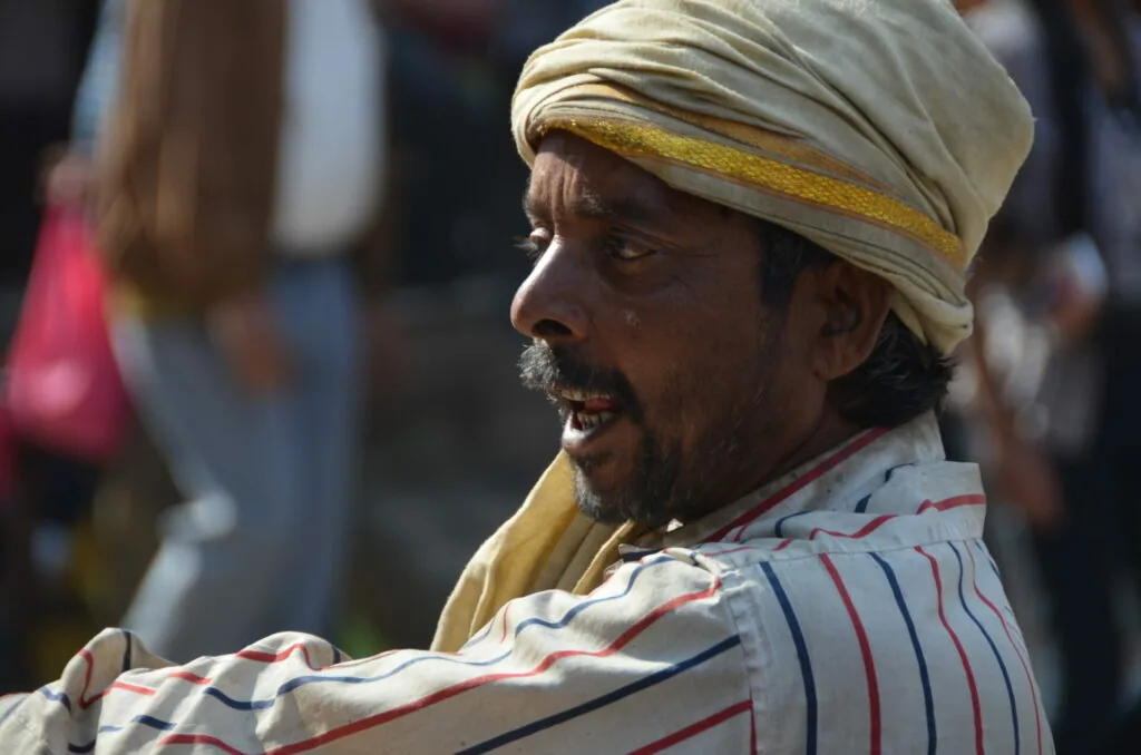 Man wearing cream-colored turban with gold stripe and striped shirt smiling at outdoor gathering