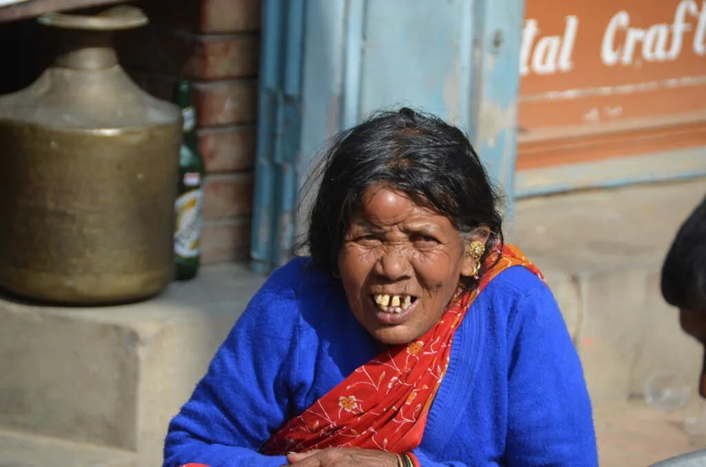 Woman in bright blue garment with red scarf smiling at camera in outdoor setting