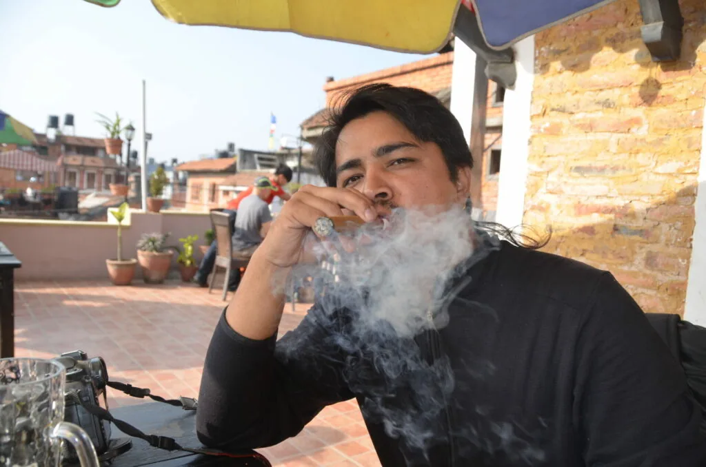 Person smoking on a rooftop terrace with urban buildings visible in the background