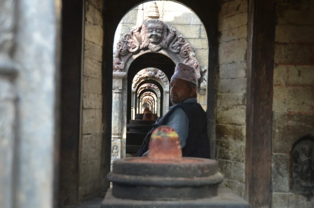 Person walking through ornate stone archway with decorative carved head at entrance, receding perspective of multiple arches