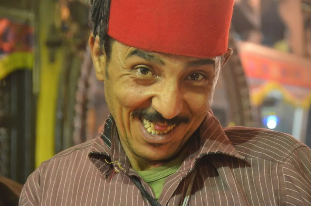 Man with distinctive mustache wearing red fez cap and brown pinstriped shirt