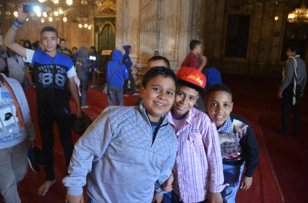 Group of young people smiling at camera inside ornate hall with high ceilings and decorative lighting