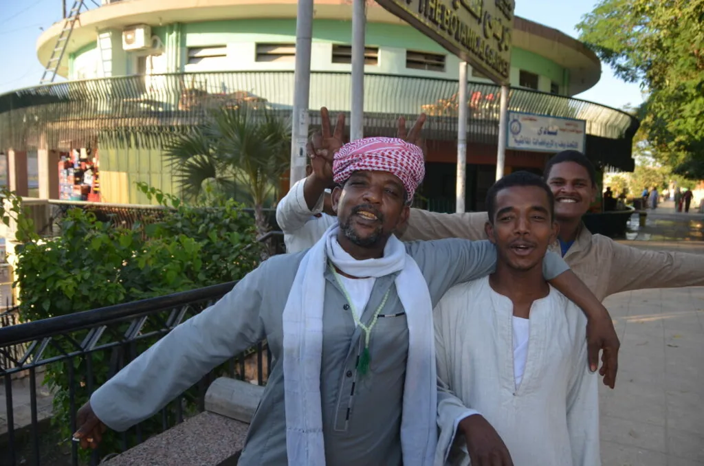 Three men posing together outside a circular building with traditional Middle Eastern architecture and dress