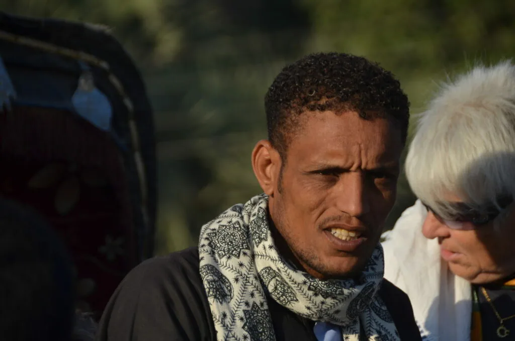 Two people conversing outdoors, one wearing a patterned scarf, with blurred natural background