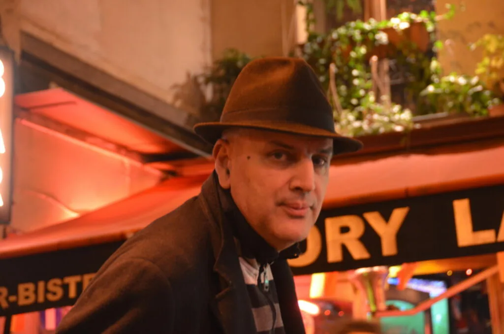 Man wearing brown cowboy hat and dark jacket in front of illuminated orange neon signage
