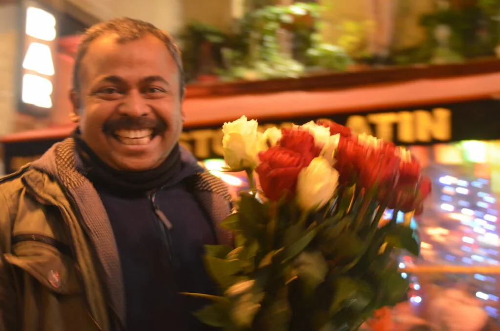 Smiling man holding red and white tulips in front of illuminated storefront