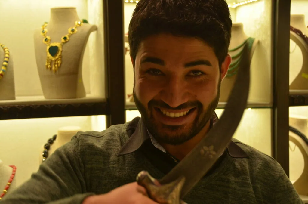 Man smiling at camera in front of illuminated jewelry display with necklaces and bracelets