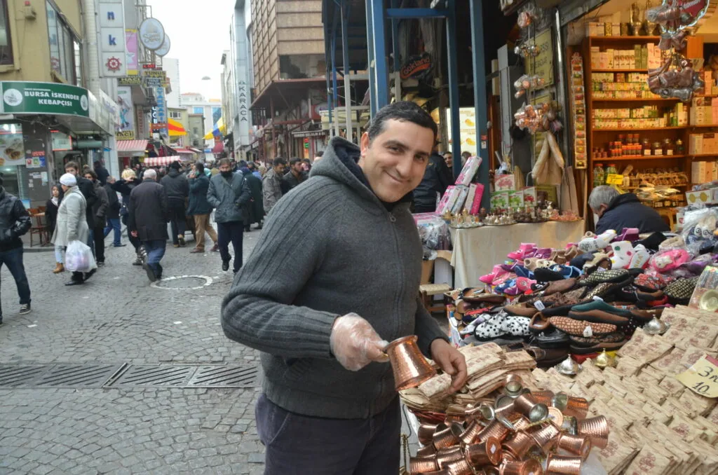 Man holding copper souvenir at street market stall with crowds and shops in urban bazaar