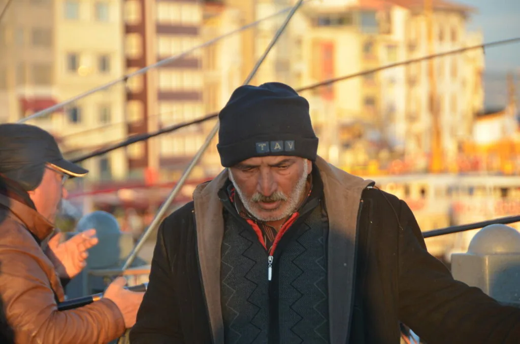 Older man wearing black beanie and brown jacket with gray collar on urban rooftop at sunset