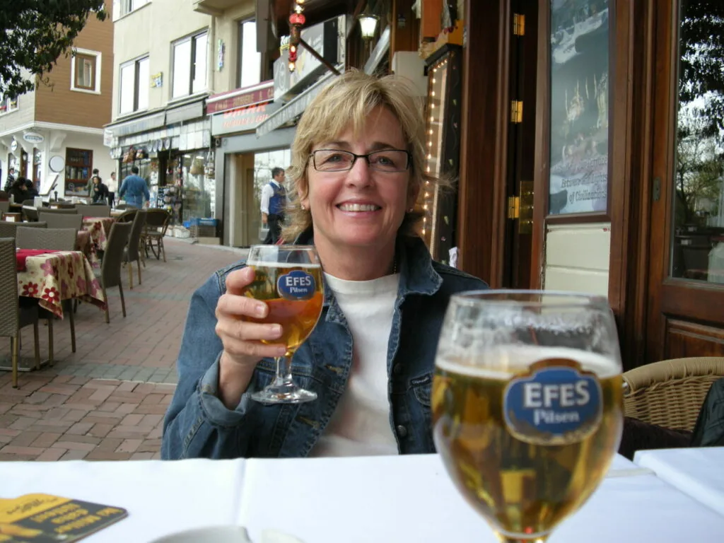 Woman wearing glasses and denim jacket holding beer glass at outdoor café table