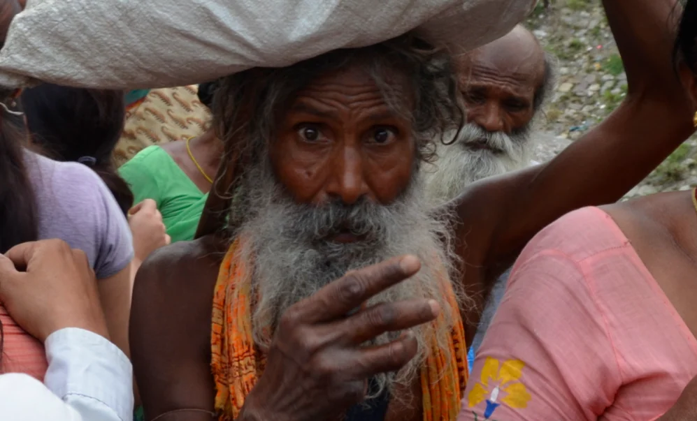 Elderly man with long white beard wearing orange cloth surrounded by people in colorful clothing