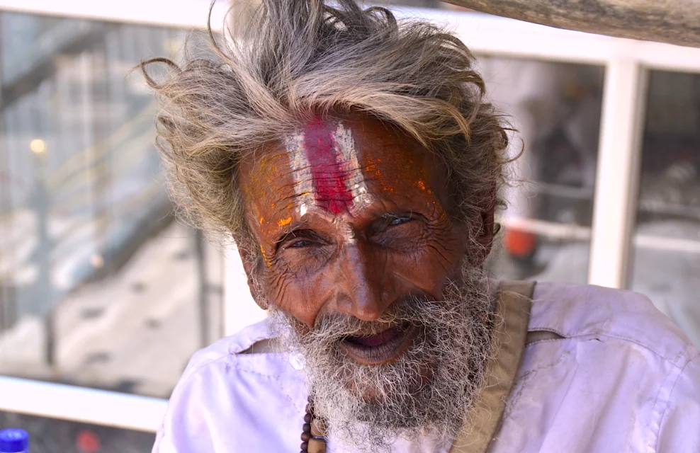 Elderly man with gray beard wearing purple shirt and religious forehead markings