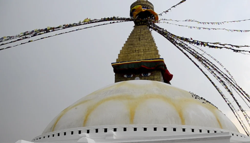 Buddhist stupa with white dome, golden spire, painted eyes, and colorful prayer flags extending from the top