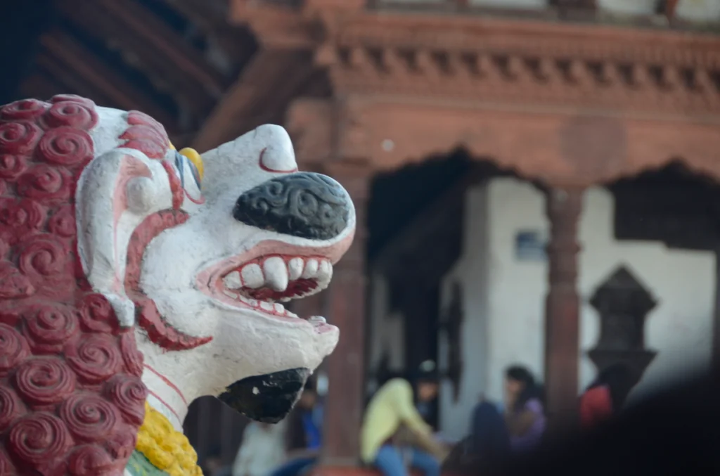 Colorful carved lion statue with red and white painted details in front of traditional Asian architecture and people
