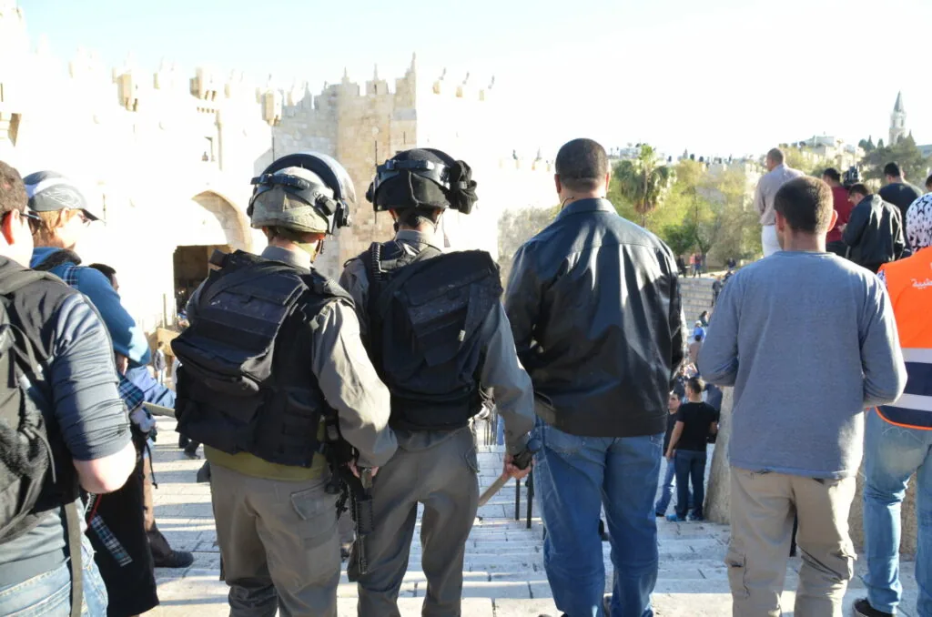 Armed police officers in tactical gear standing among civilians near ancient fortified walls and towers