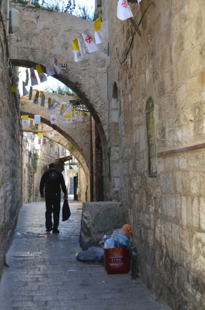 Narrow stone alleyway with arched passages, hanging decorations, and a person walking
