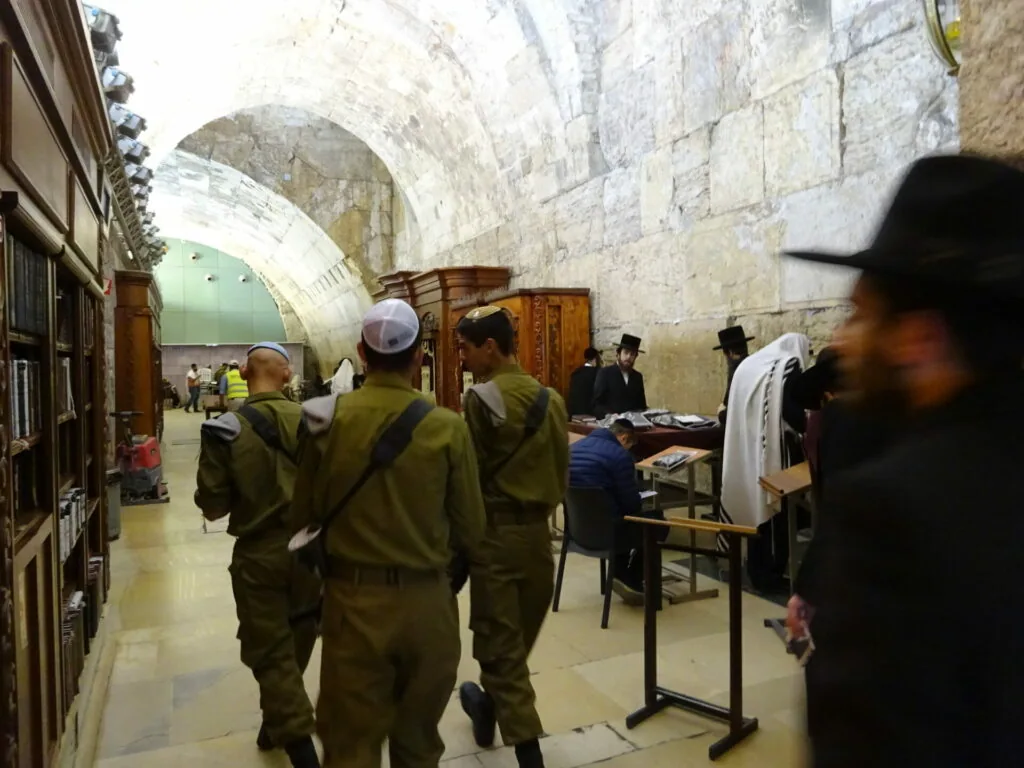 Military personnel and visitors inside a stone-vaulted underground corridor with arched ceiling