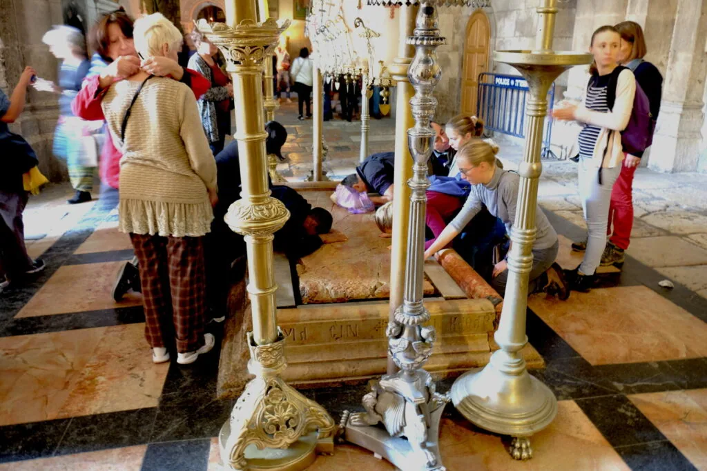 Visitors in ornate interior church space with decorative brass candelabra and checkered floor