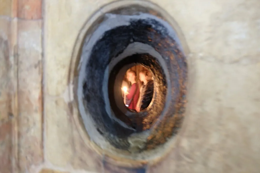 Lit candle visible through a circular opening in a weathered stone wall