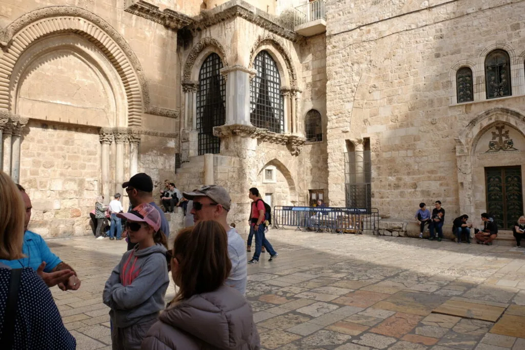 Tourists in a courtyard surrounded by ancient stone buildings with Romanesque arches and narrow windows