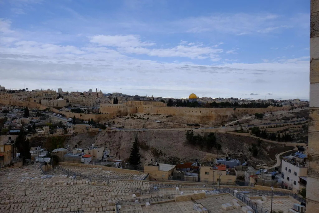 Panoramic view of Jerusalem's Old City with the Dome of the Rock visible on the horizon, surrounded by ancient stone buildings and walls