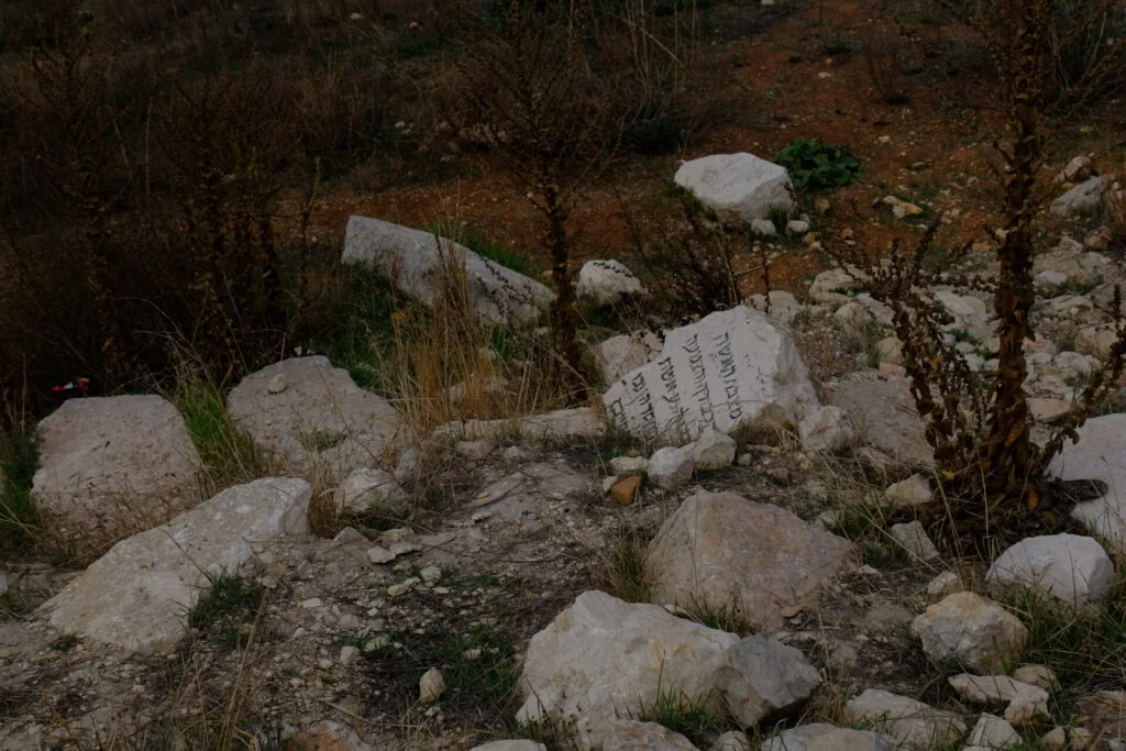 Ancient stone with carved Hebrew text among rocky terrain and sparse vegetation