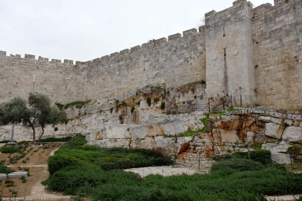 Ancient stone fortress wall with crenellations overlooking terraced gardens and olive tree