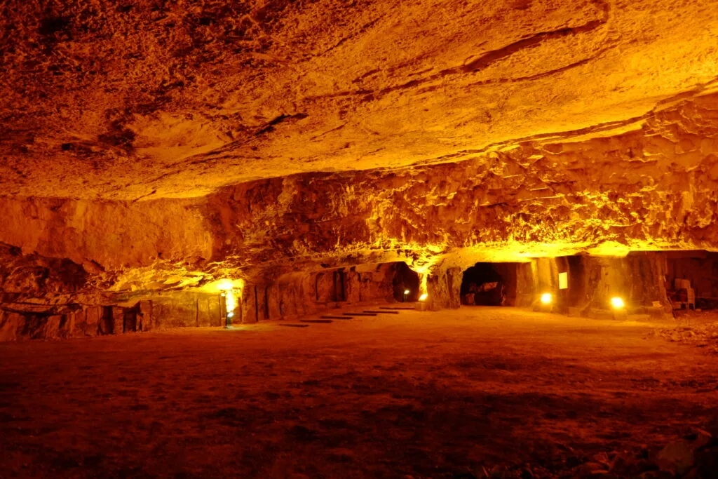 Underground cavern with golden-amber lighting illuminating rock walls and floor with carved openings
