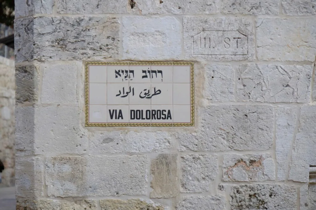 Street sign on white stone wall reading Via Dolorosa in Hebrew, Arabic, and English