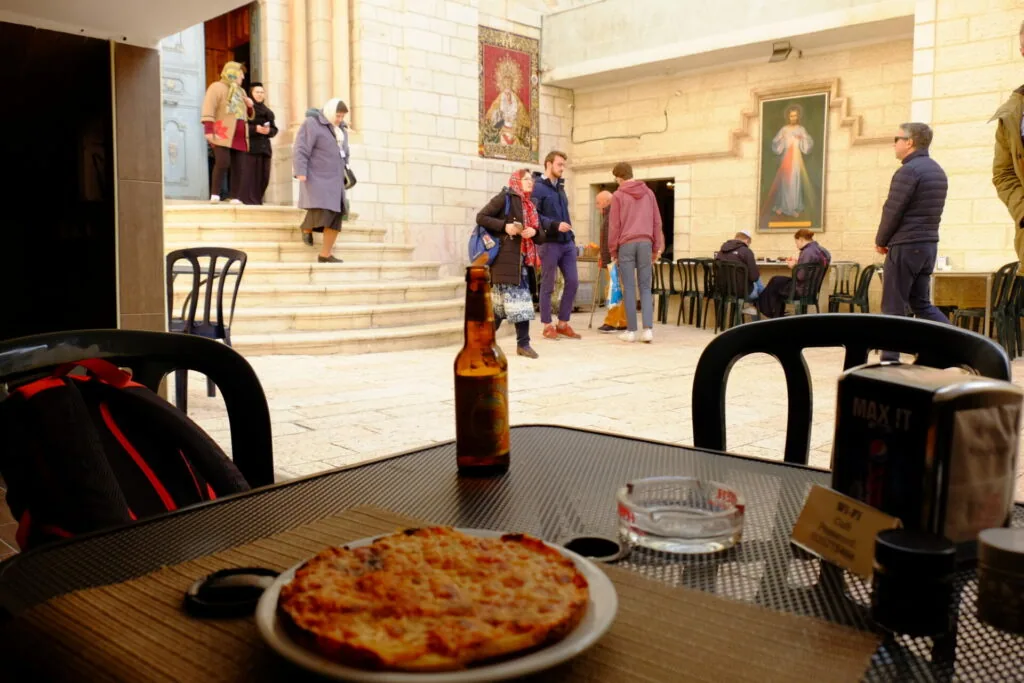 Pizza on table in foreground with people gathering in church interior with religious artwork and white tile walls