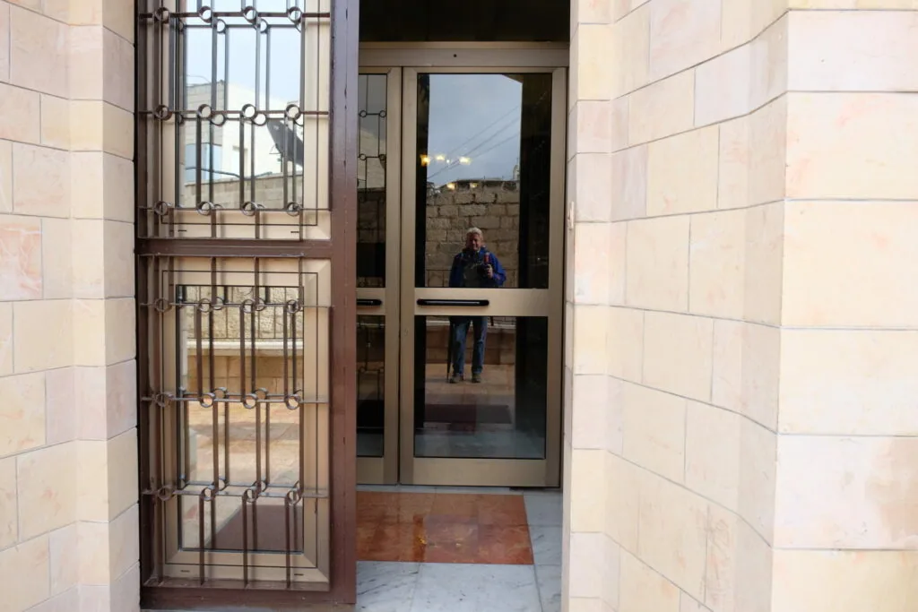 Person visible through glass door entrance with metal security gate and stone walls on either side