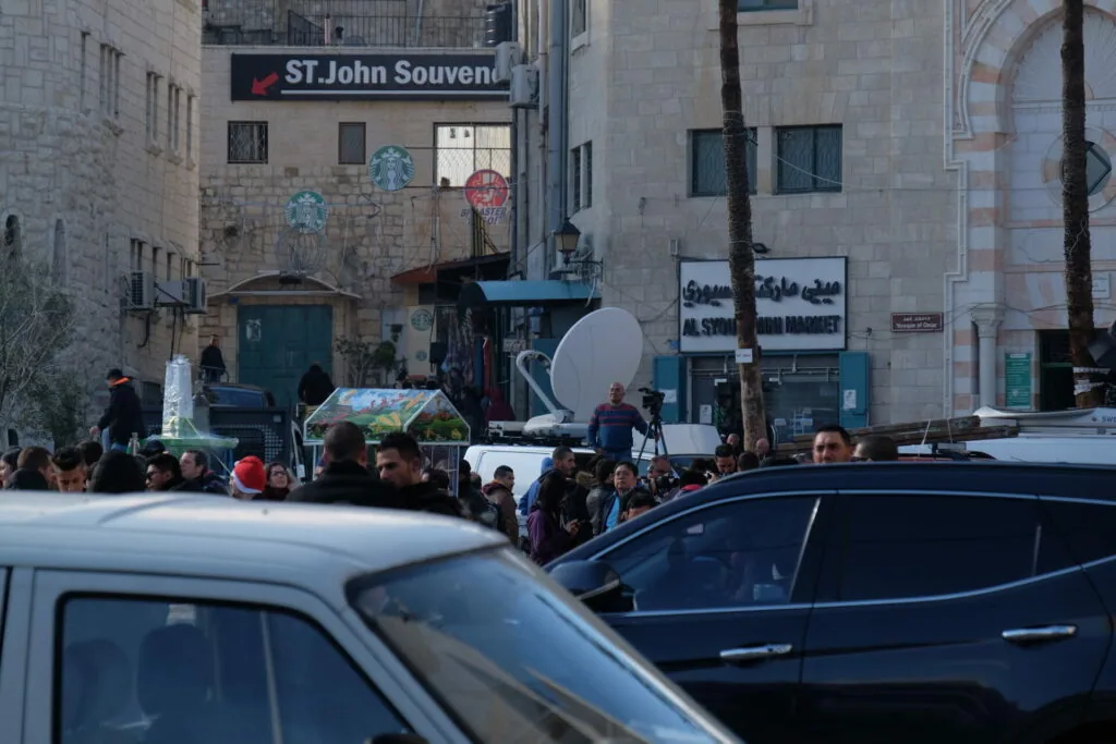 Busy street scene with parked cars, pedestrians, and stone buildings with St. John Souvenir shop sign visible