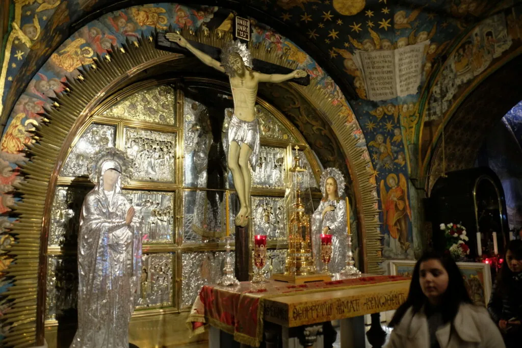 Orthodox church interior with ornate golden arch, crucifix, and religious iconography with worshipper in foreground