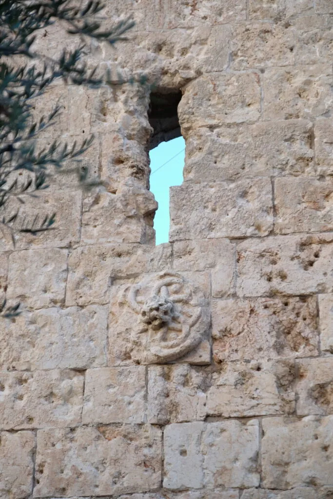 Narrow vertical opening in ancient stone wall with carved ornament detail below, bright blue sky visible through gap
