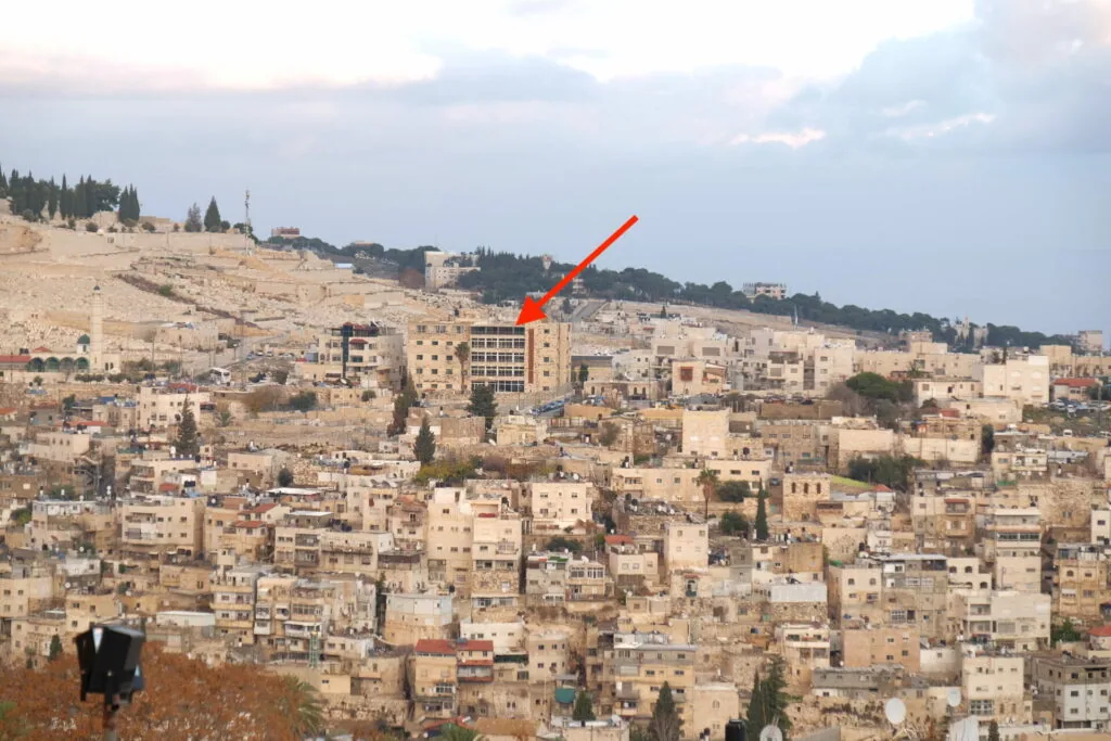 Hillside cityscape with dense tan stone buildings and a red arrow pointing to a multi-story structure