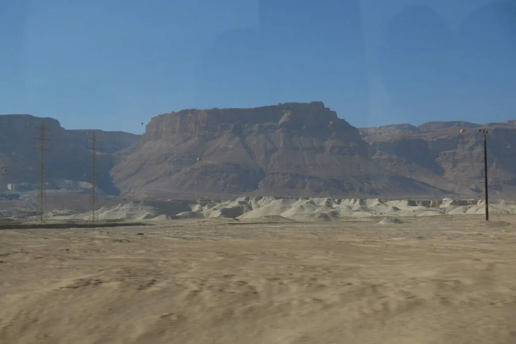 Desert landscape with layered brown mountains and utility poles under clear blue sky
