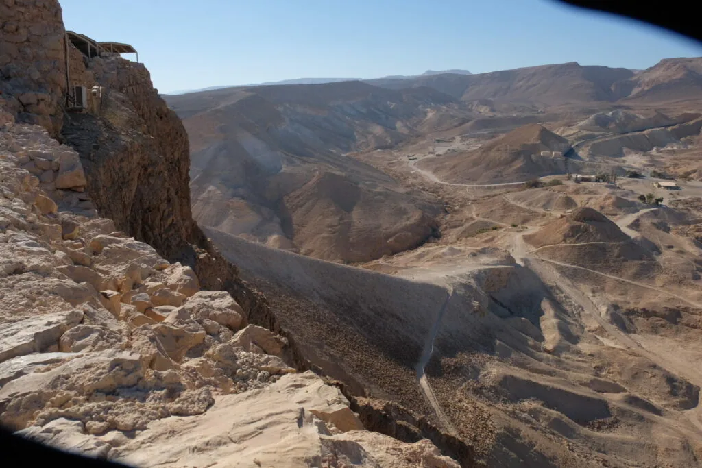 Rocky desert mountain landscape with steep cliffs and winding roads through arid valleys below.
